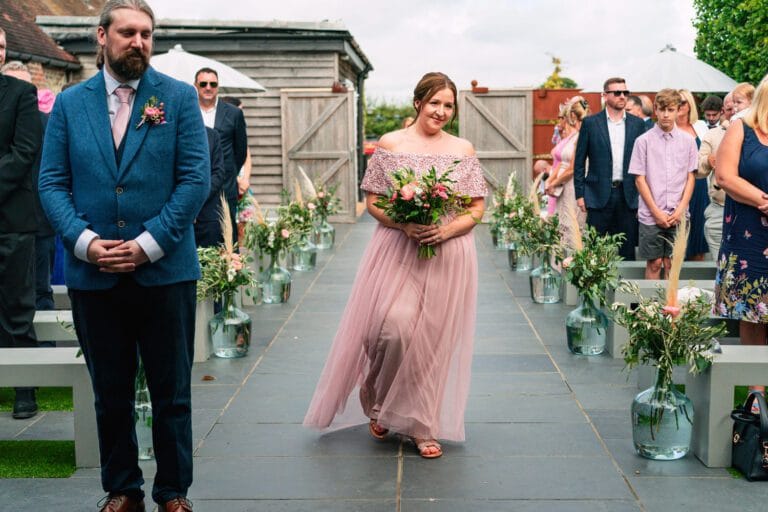 bridesmaid-walking-into-wedding-ceremony-at-southend-barns